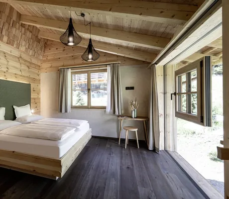 Modern eingerichtetes Schlafzimmer mit vielen Holzelementen, Doppeltbett und bodentiefer Fensterseite in den Südtirol Chalets Valsegg