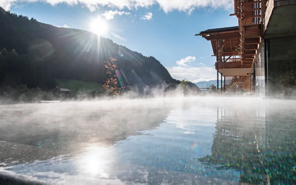 Blick auf den beheizten Outdoor-Infinitypool der Südtirol Chalets Valsegg während die Sonne hinter den Bergen hervorkommt