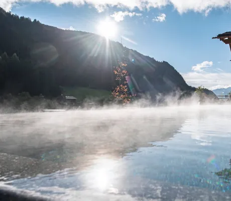 Blick auf den beheizten Outdoor-Infinitypool der Südtirol Chalets Valsegg während die Sonne hinter den Bergen hervorkommt