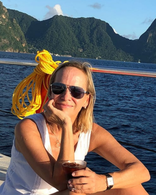 Autorenporträt Christine Paasche mit Sonnenbrille sitzend auf einem Boot mit Meerkulisse und Bergkette