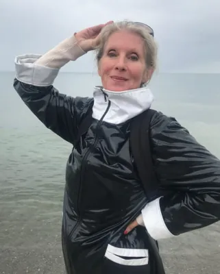 Autorenporträt Hanne Bahra in schwarz-weißem Lackmantel stehend vor Meerkulisse