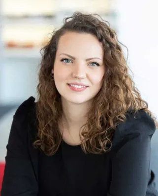 Autorenporträt Katharina Gruber lächelnd mit lockigem Haar und schwarzem Oberteil