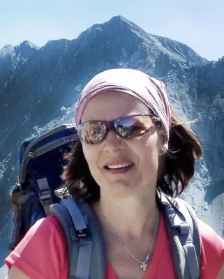 Autorenporträt Kirsten Posautz mit Sonnenbrille und Rucksack vor Bergen stehend