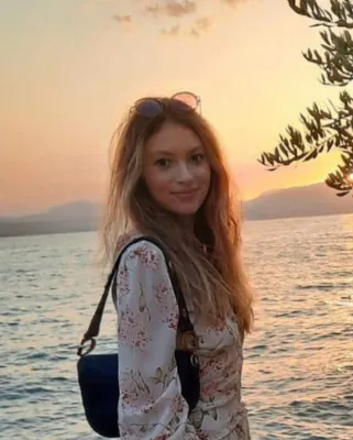 Autorenporträt Leonie Schwenda steht lächelnd mit Blumenkleid vor einem See mit Bergkulisse