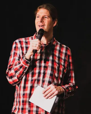 Autorenporträt Michael Noghero in Karohemd beim moderieren mit Mikro und Moderationskarte