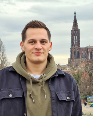 Autorenporträt Niklas Ramminger steht lächelnd vor Stadtkulisse mit Dom