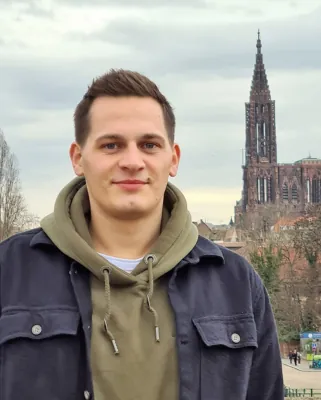 Autorenporträt Niklas Ramminger steht lächelnd vor Stadtkulisse mit Dom