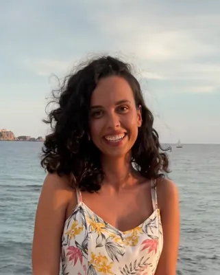 Sarah Arzberger steht lachend mit Blumenkleid vor Meer