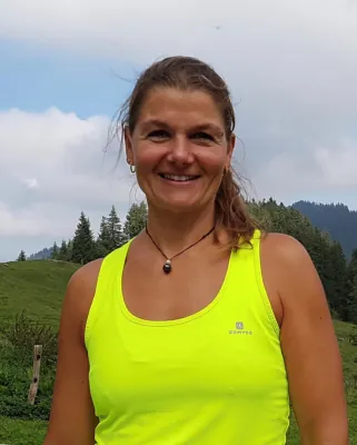 Autorenporträt Silvia Schwendtner steht lächelnd mit Neon-Shirt vor bewaldeten Bergen