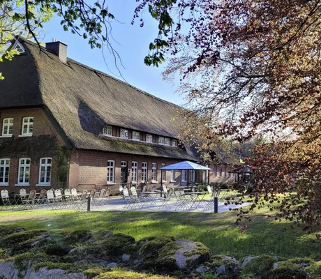 reetgedeckte Scheune hinter bestuhlter Terrasse mit Sonnenschirm im Gut Thansen