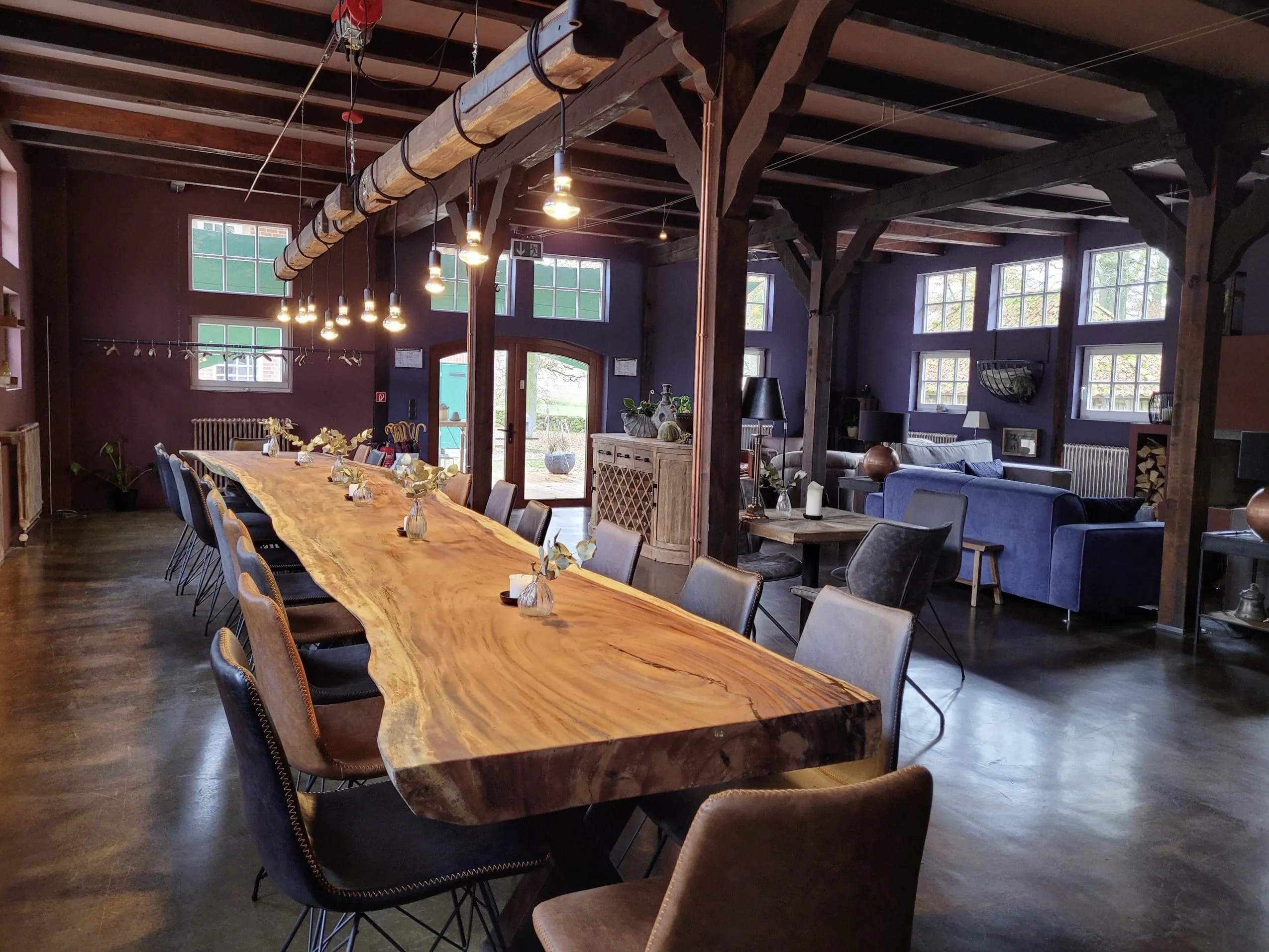 sehr langer Holztisch unter dem Dach mit vielen Lampen an einem Balken in Gut Thansen