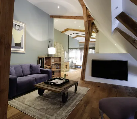 Suite unter dem Dach mit alten Balken, lila Sofa und modernem Porträt in Gut Thansen