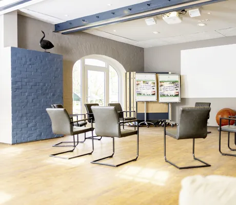 Stuhlkreis mit grauen Ledersesseln und blau gestrichenem Wandelement im Tagungsraum des Gut Thansen