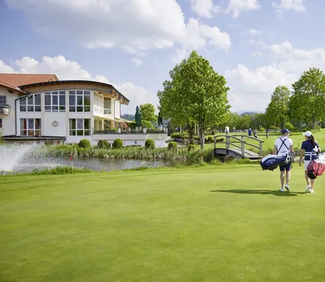 Mann und Frau in Rückenansicht mit Golfoutfit spazieren über die Golfanlage des Hanusel Hof