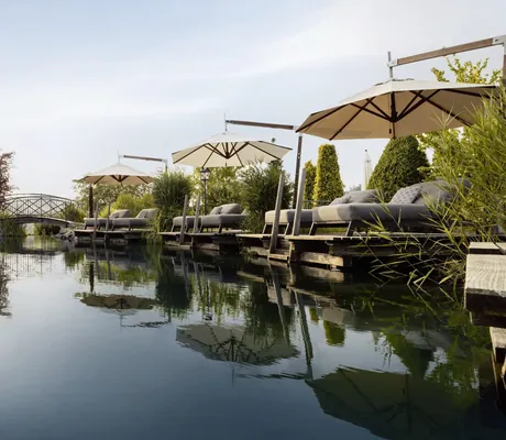 gepolsterte Liegen am Naturbadesee auf Pontons mit augespannten beigen Sonnenschirmen im Wellnesshotel Jagdhof Röhrnbach