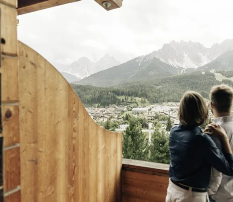umarmtes Paar auf dem Holzbalkon des Naturhotel Leitlhof schaut auf Innichen