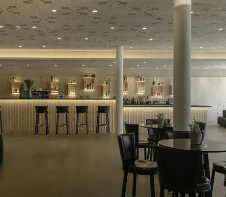 hölzerne Bar mit schwarzen Barhockern und runden Tischen davor im Naturhotel Leitlhof