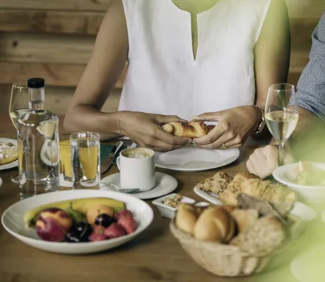 Frau in weißem Shirt bricht ein Croissant am Frühstückstisch im Naturhotel Leitlhof