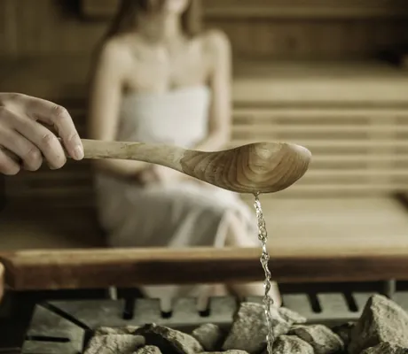 Wasser wird für den Aufguss in der Sauna mit dem Holzlöffel auf die Kohlen gegossen im Naturhotel Leitlhof