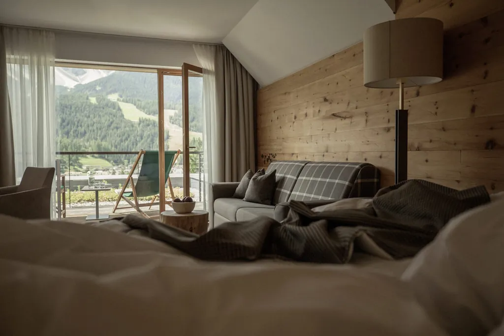 Blick vom Bett aus auf den Balkon mit grünem Liegestuhl und Skipiste im Naturhotel Leitlhof