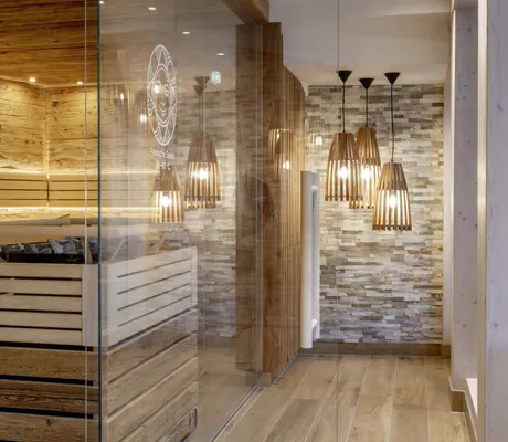 Sauna mit Sonnenlogo des Sonnenalp Resort auf der Glastür und Holz-Hängeleuchten