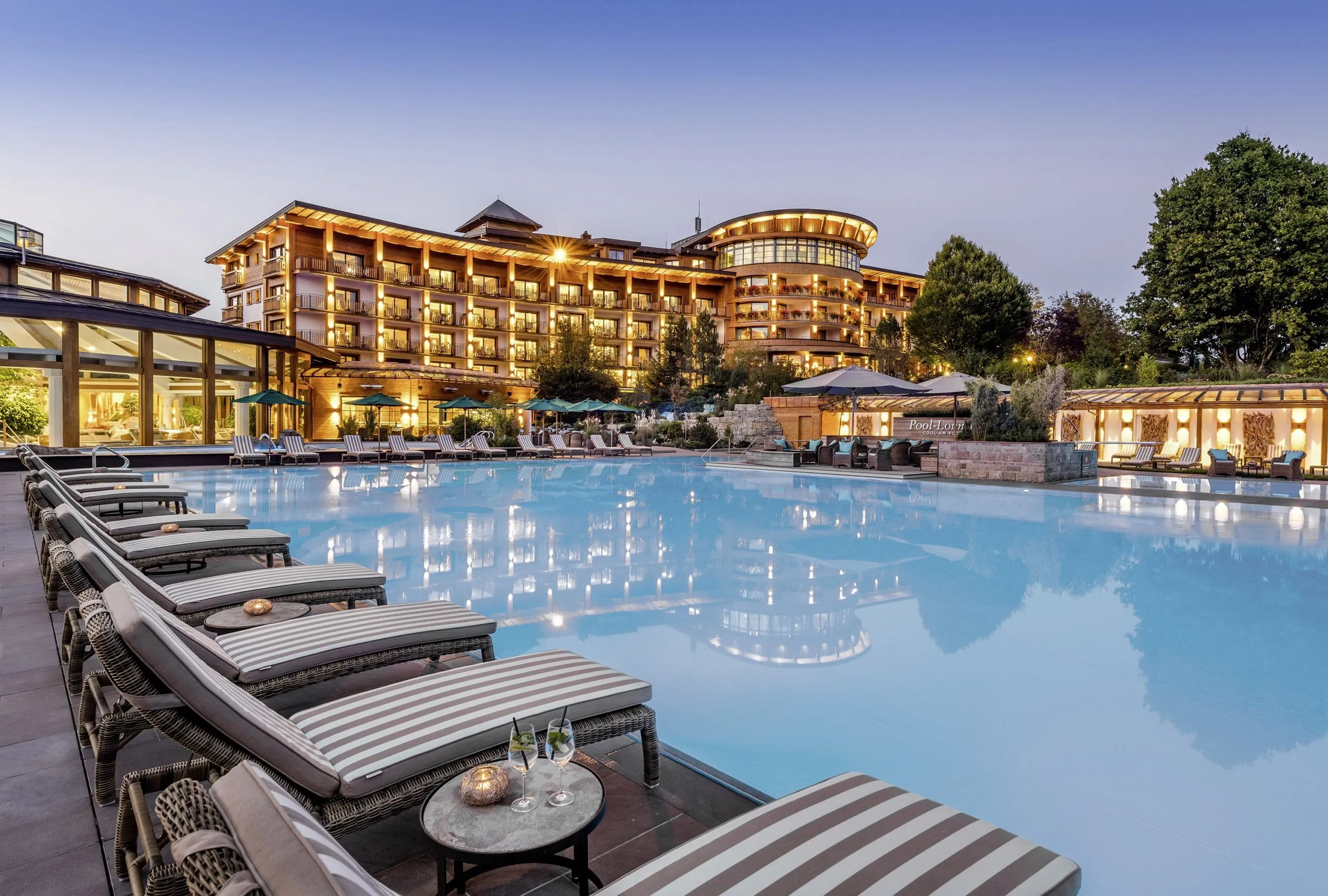 Sonnenliegen mit gestreiften Polstern am Beckenrand des Outdoorpools des Sonnenalp Resort