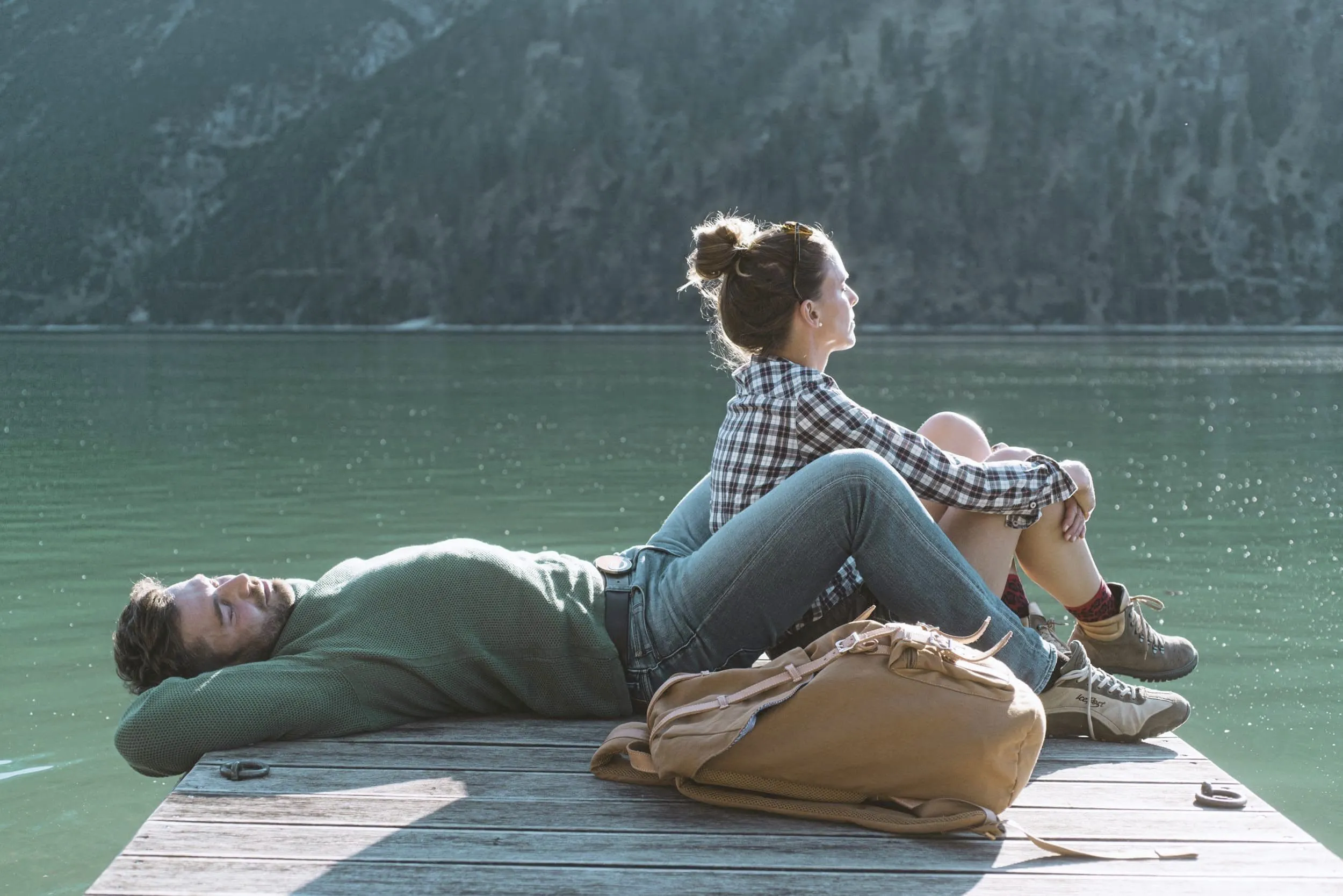 Mann liegend und Frau sitzend auf einem Steg am Achensee mit braunem Rucksack