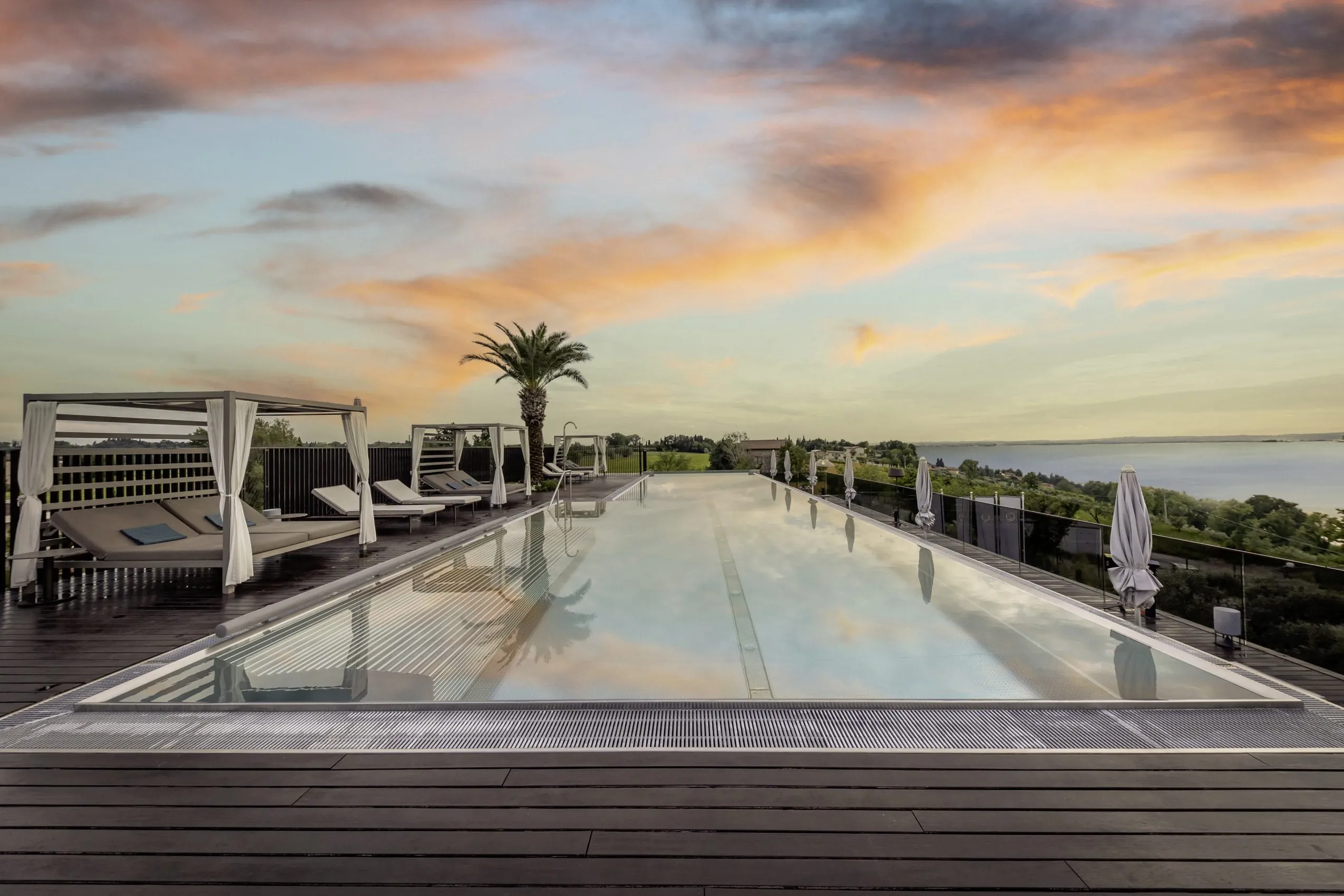 Skypool mit Blick auf den Gardasee in der Abendd&auml;mmerung mit rotem Himmel im Quellenhof Luxury Resort Lazise