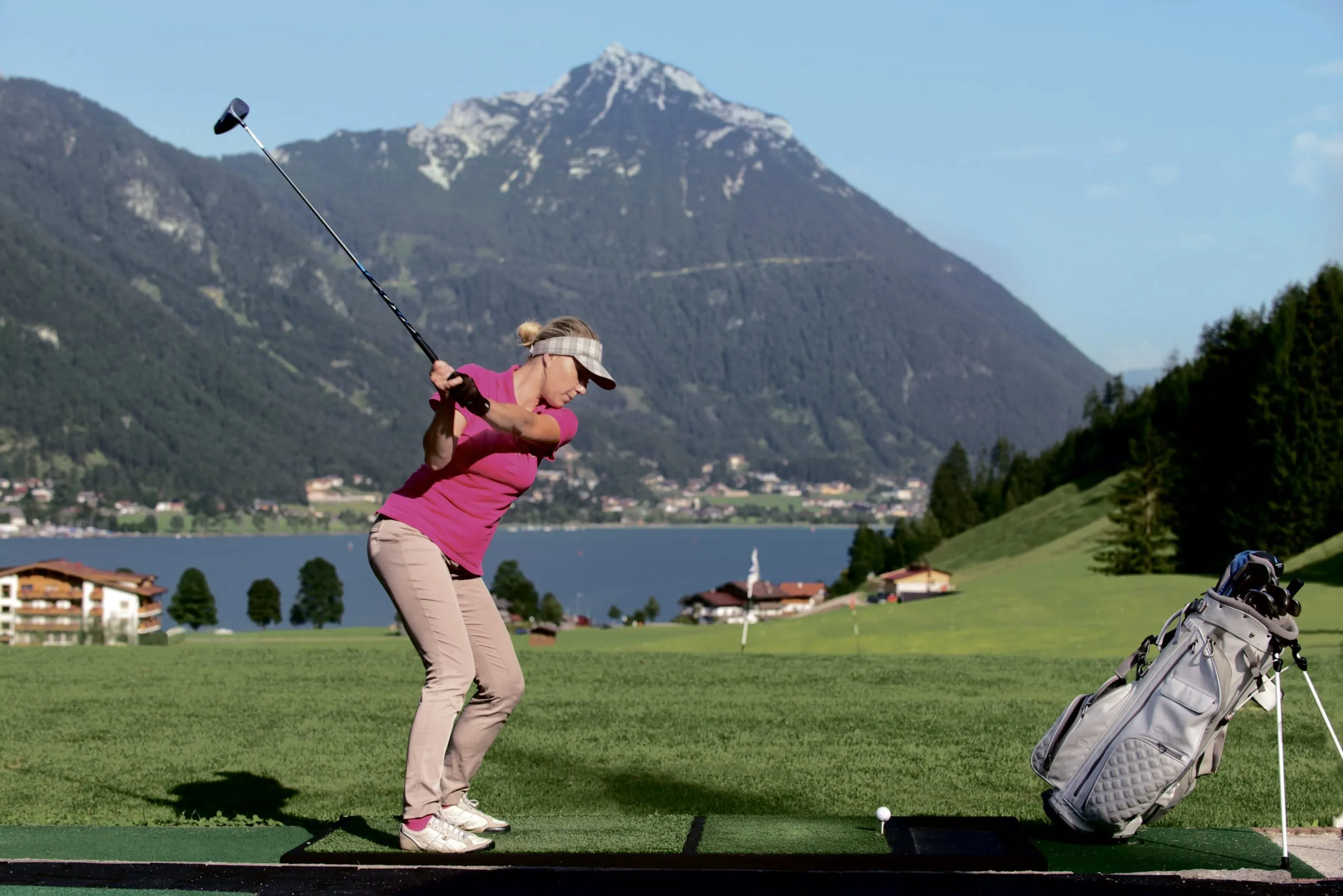 Frau in rosa Outfit schl&auml;gt gerade einen Golfball auf dem Golfplatz am Travel Charme F&uuml;rstenhaus am Achensee