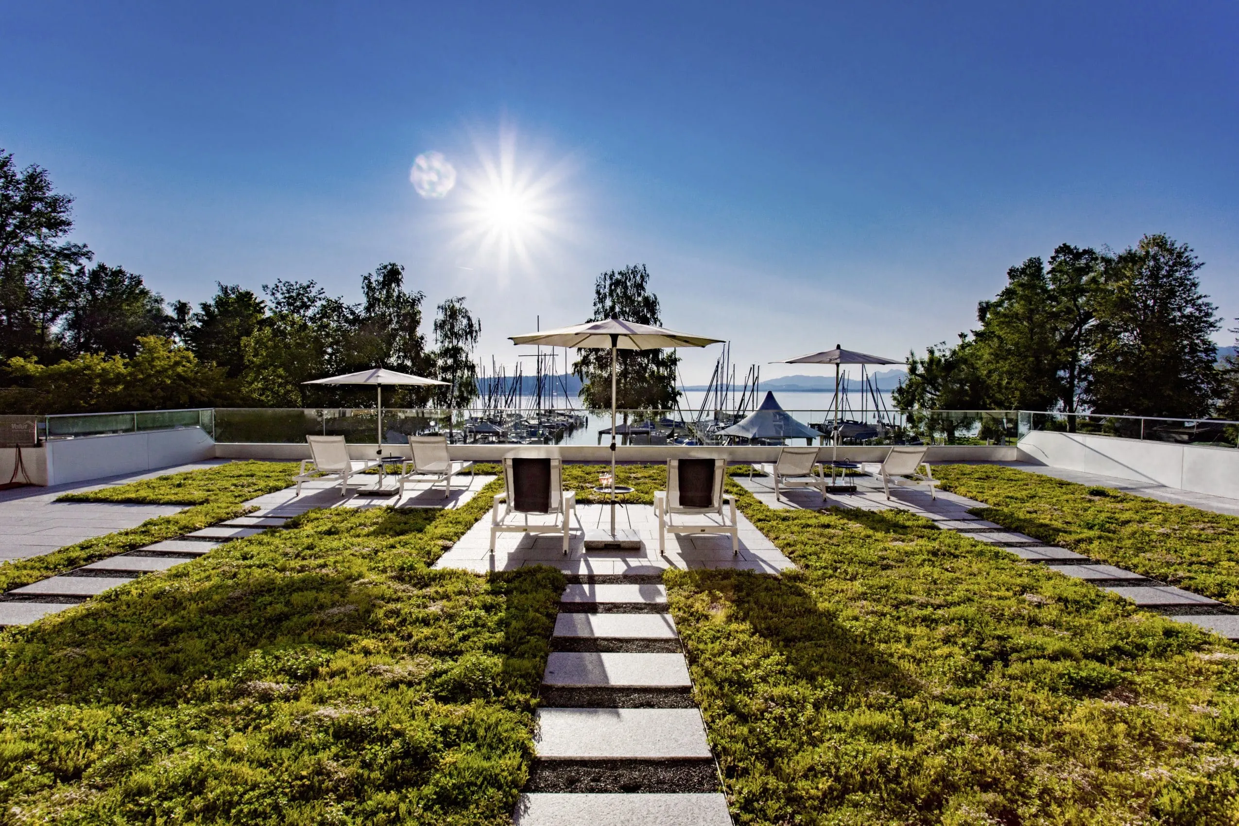 Liegest&uuml;hle auf Steinplattformen im Garten des Yachthotel Chiemsee mit Blick auf den See