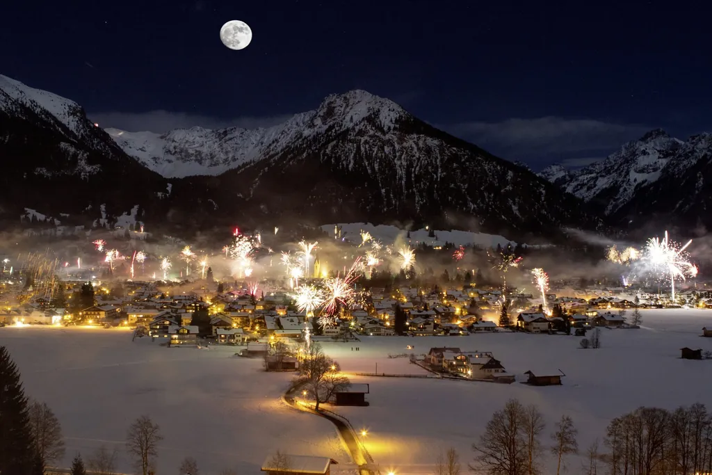Bergdorf vor schneebedeckten Gipfeln mit Silvesterfeuerwerk