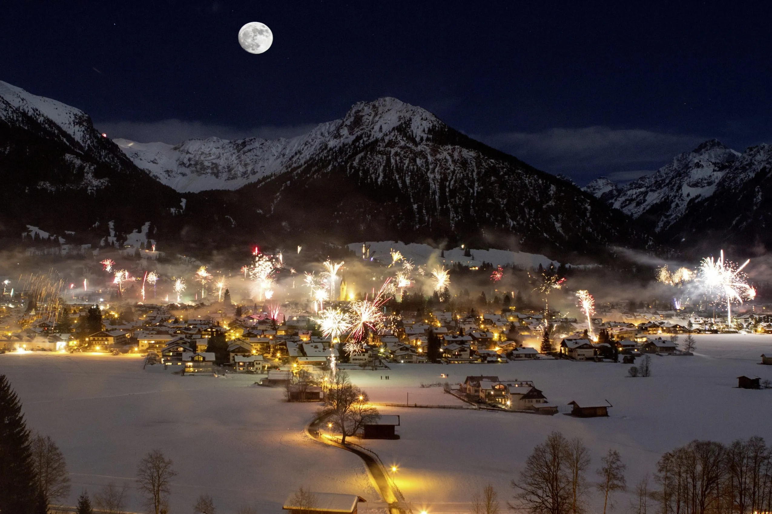 Bergdorf vor schneebedeckten Gipfeln mit Silvesterfeuerwerk