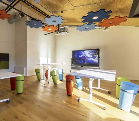 Tagungsraum Creative Flow mit Parkettboden, bunten hohen Sitzhockern und Deckenbeleuchtung in Zahnrad-Optik-