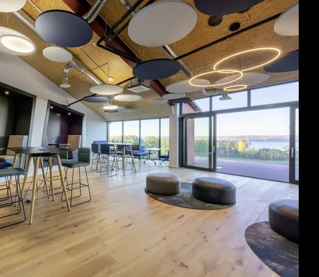 Tagungsraum Co-Working im Lounge-Stil mit Neon-Scheiben-Deckenbeleuchtung, bodentiefen Terrassenfenstern und Seeblick