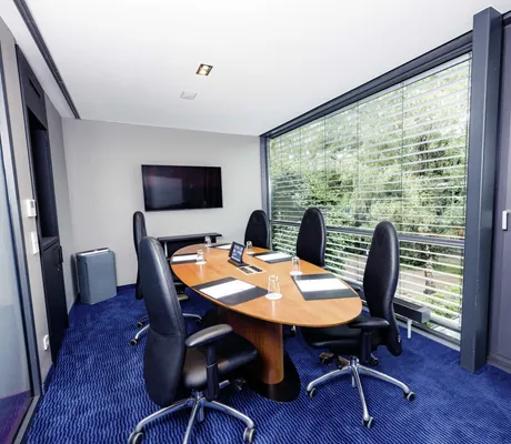 Ovaler Tagungstisch mit vier gepolsterten Bürostühlen und Wandscreen vor Fensterwand im Tagungsraum Klee