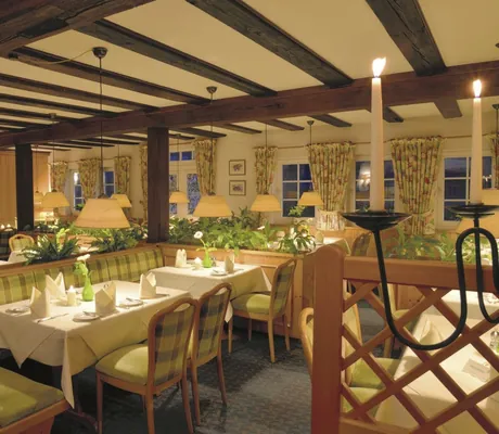 Restaurant mit rustikaler Holzbalkendecke, stoffkarobezogenen Holzstühlen, Blümchenvorhängen und brennenden Kerzen