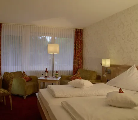 Illuminiertes Doppelzimmer mit Sitzgruppe vor einer Fensterfront in Grünen