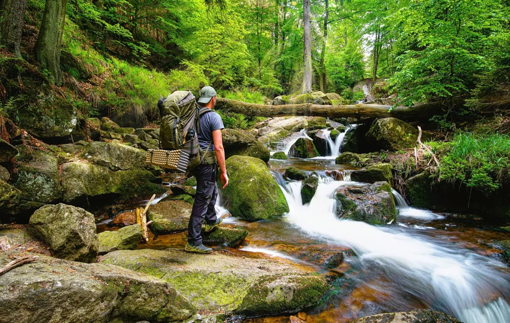 Wanderer mit Rucksack steht im Wald vor den Ilsefällen im Harz