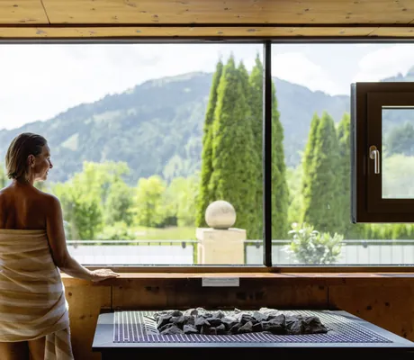 in gelb gestreiftes Handtuch gewickelte Frau steht am Fenster der Sauna im A-ROSA Kitzbühel