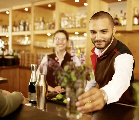 Barista stellt an der Bar im Hotel Oberstdorf einen Kräuter-Rührtail auf die Theke