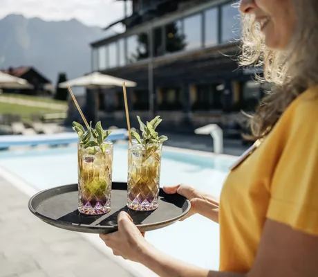 Servicekraft serviert zwei Botanicals/Rührtails am Aussenpool