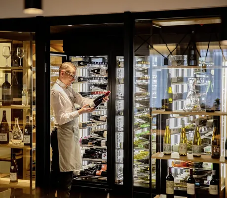 Sommelier mit grauer Schürze prüft Weinflasche in der Vinothek des Pfalzblick Wald Spa Resort