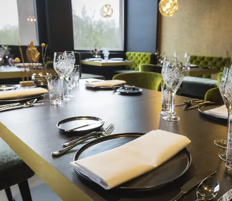 eingedeckter Tisch im Restaurant der Bornmühle vor grasgrün gepolsterten Stühlen