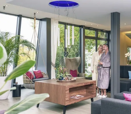 Paar im Bademantel im Spabereich mit Bücherregal, Hängesessel und Sofa im Hotel Heinz