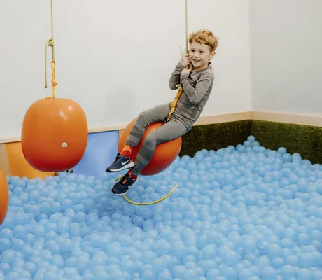 rothaariger Junge schwingt auf orangem Ball über dem Bällebad im Das Mühlwald