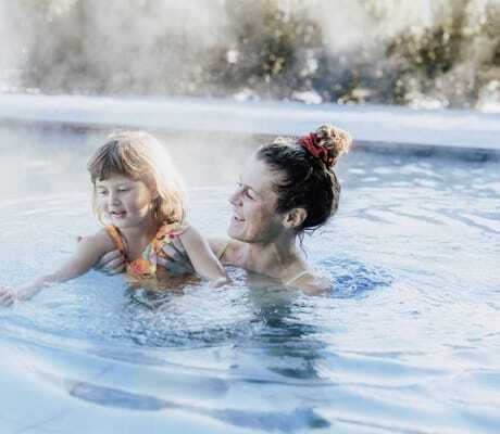 Frau mit Dutt hält kleines Mädchen im Schwimmbecken des Das Mühlwald