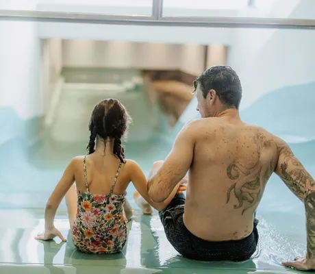 tätowierter Vater rutscht mit Tochter im Badeanzug die Wasser-Wellenrutsche im Das Mühlwald hinunter