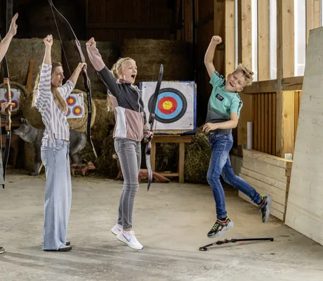 Familie mit zwei Jugendlichen springt beim Bogenschießen freudig in die Luft