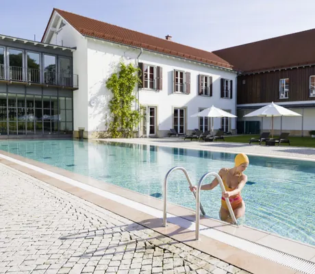 Junge Frau mit Badekappe steigt in den Outdoorpool ein