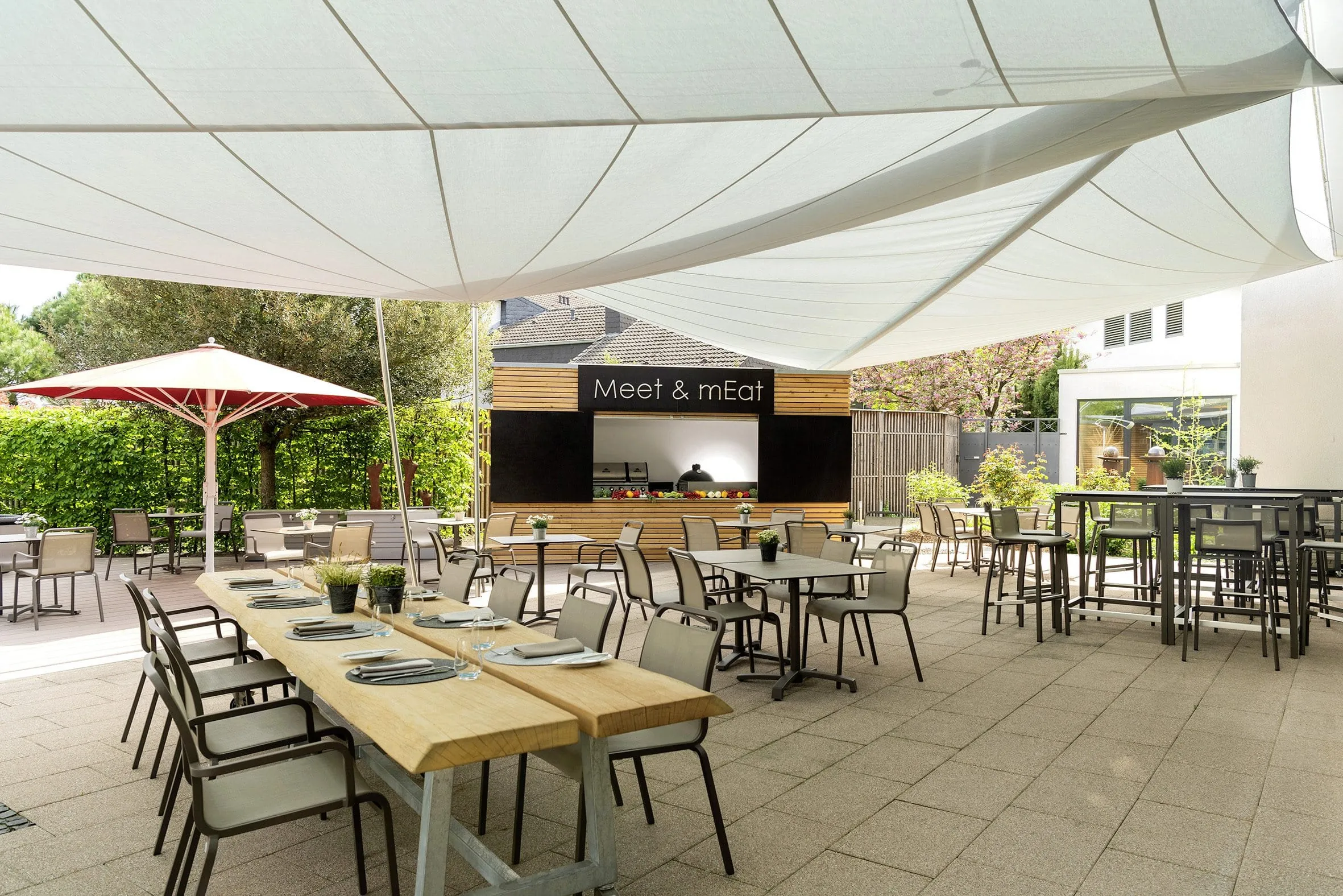 Terrasse des Atrium Holz Mainz mit Grillh&uuml;tte und gedeckten Tischen unter Sonnensegel